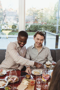 Smiling men having food with friend at table in restaurant