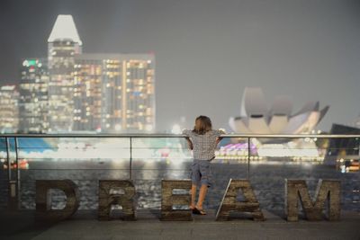 Rear view of girl standing against illuminated cityscape