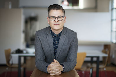 Portrait of confident businessman leaning on wooden table at office