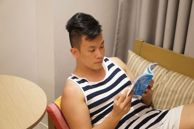 Man reading book while leaning on sofa at home