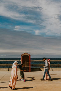 Rear view of friends enjoying at sea shore against sky