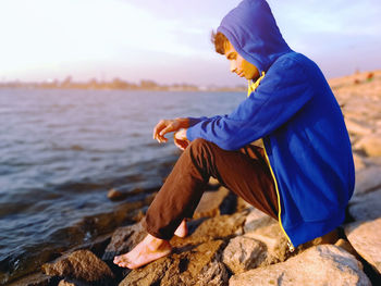 Side view of young woman sitting on rock by sea