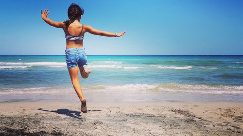 Rear view of shirtless woman standing on beach against clear sky