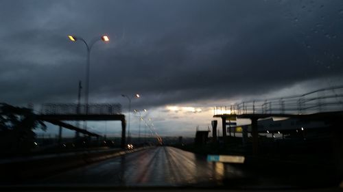 Illuminated road against cloudy sky