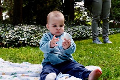 Full length of cute baby boy holding paper while sitting on picnic blanket in park