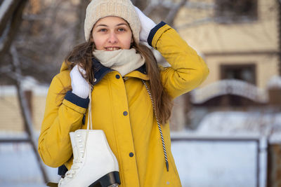 Portrait of young woman in yellow jacket with ice skates goes to rink