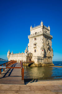 Buildings by sea against clear blue sky