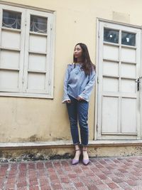 Portrait of young woman standing against building