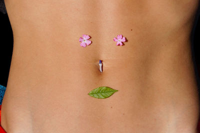 Midsection of woman with flowers and leaf on abdomen