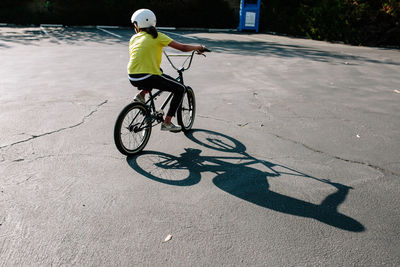 Back of a girl and her shadow riding a bmx bike in a parking lot