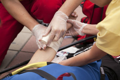 Cropped hands of people bandaging man indoors