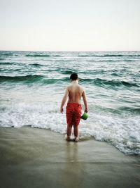 Rear view of shirtless man standing on beach against clear sky