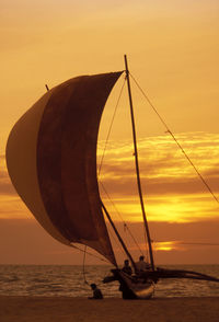 People on boat at beach against sky during sunset