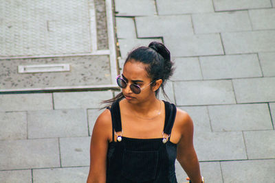 Young woman wearing sunglasses standing against brick wall