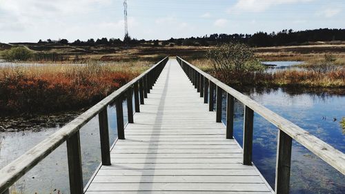 Empty wooden bridge over calm lake against sky