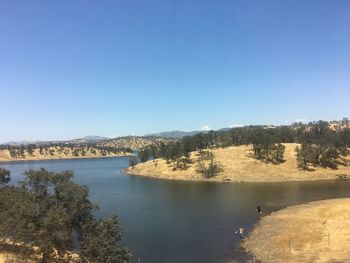 Scenic view of river by mountains against clear blue sky