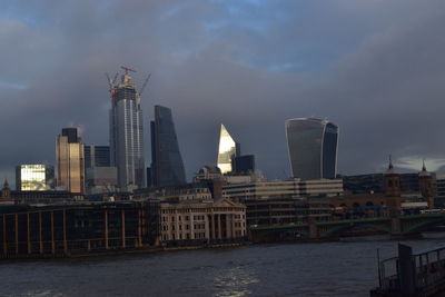 Modern buildings by river against sky in city