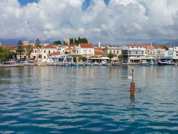 Sailboats in sea by buildings in city against sky