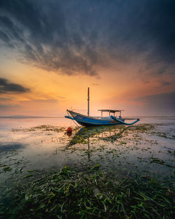 Fishing boat on beach against sky during sunset