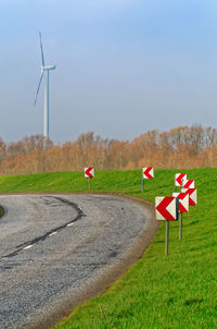 Scenic view of country road and wind turbines against sky
