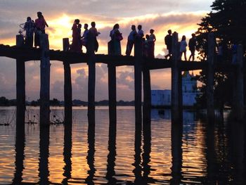 Silhouette people looking at lake against sunset sky