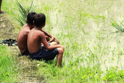 Rear view of shirtless boy sitting on field
