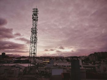 Cranes against buildings in city at sunset