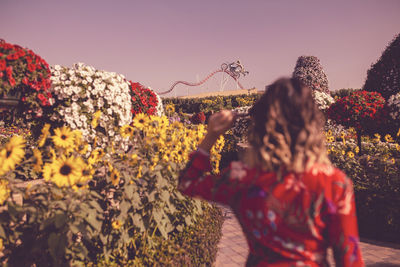 Rear view of women standing by flowering plants against sky
