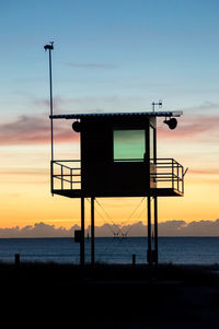 Scenic view of silhouette lookout tower on beach against cloudy sky