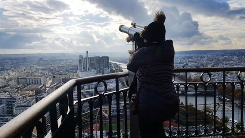 Rear view of woman looking at cityscape through coin-operated binoculars from eiffel tower