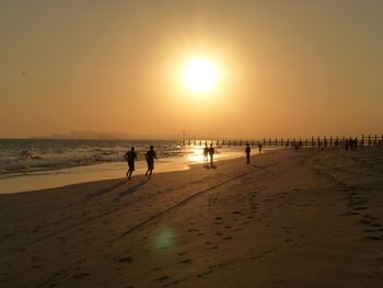 Silhouette people on beach against sky during sunset