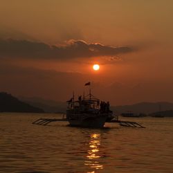 Silhouette fishing boat in sea against sky during sunset