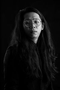 Portrait of young man standing against black background