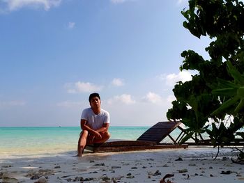 Full length portrait of young man sitting on beach