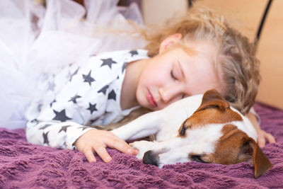 A  little girl in pajamas with asterisks and a dog jack russell sleep together in an embrace. 