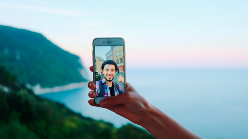Portrait of woman photographing through mobile phone against sky
