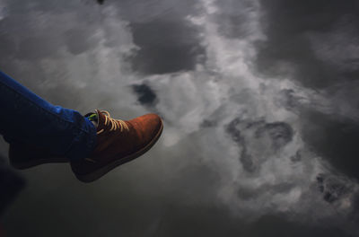 Low section of man over water with reflection of clouds