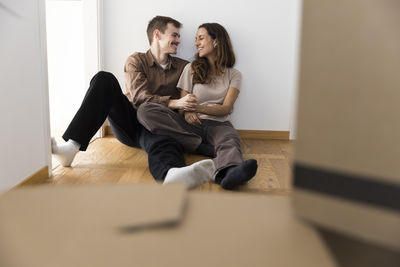 Happy multiracial couple with hands intertwined sitting on hardwood floor at home