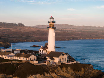 Lighthouse by sea against sky during sunset
