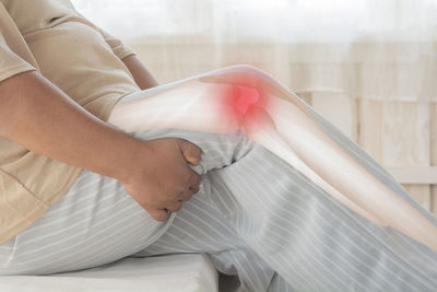 Low section of woman sitting on bed at home