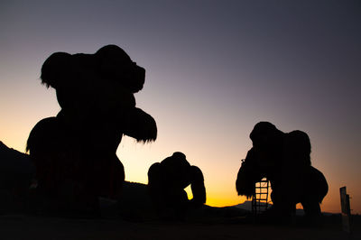 Silhouette people by statue against sky during sunset