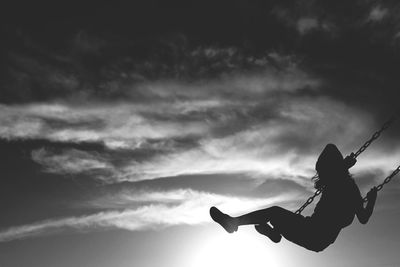 Low angle view of silhouette girl swinging on swing against sky