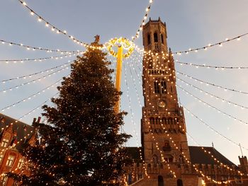 Low angle view of belfort tower and a christmas tree against sky at dusk in bruges