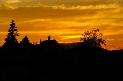 Silhouette trees and buildings against orange sky