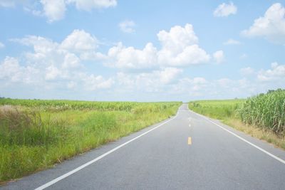 Empty road amidst field against sky