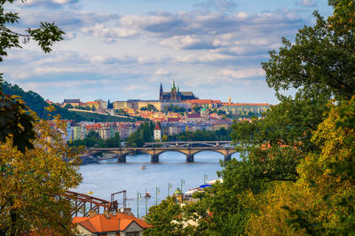 Bridge over river by buildings in city against sky