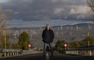 Adult man standing on asphalt road looking at view of modern windmills. almeria, spain