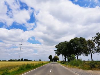 Road amidst trees on field against sky