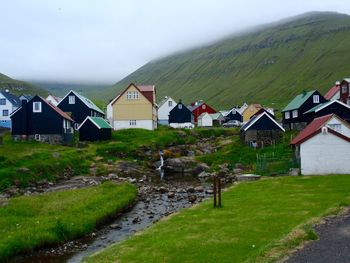 Houses on field by buildings against sky