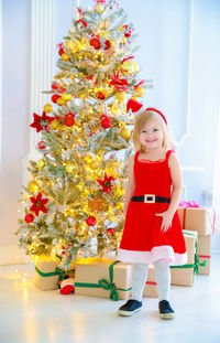 Full length portrait of girl standing against decorated christmas tree